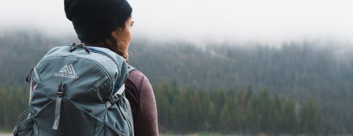 A woman with a backpack on looking into the distance towards a lake and a forest.