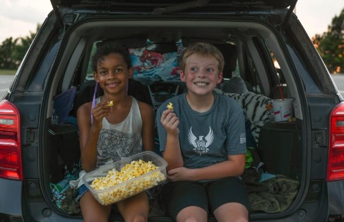 Two Kids enjoying popcorn while watching a movie outside in the back of a car.