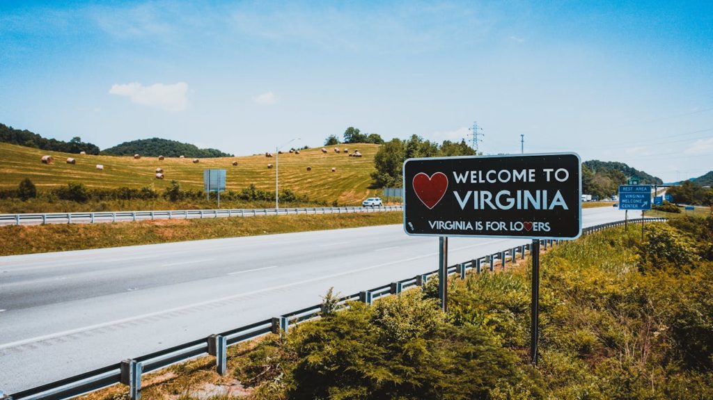 A sign welcoming new arrivals to Virginia, blue sky, greenery, and hay rolls.